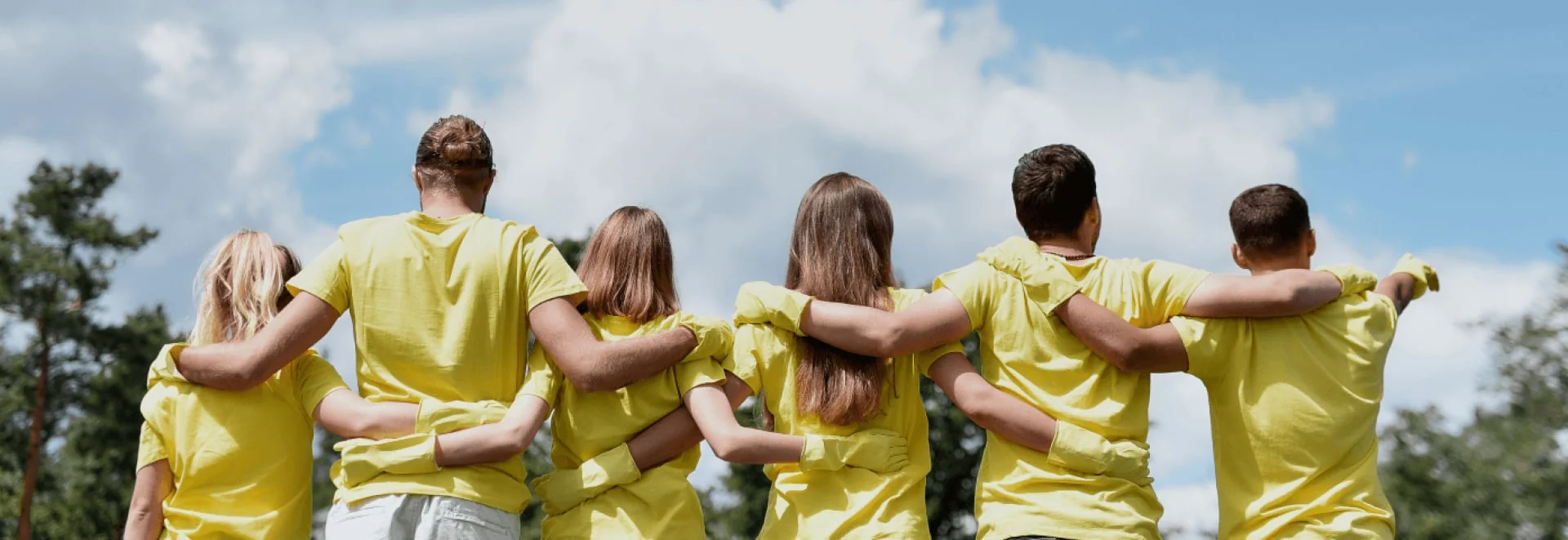 Group of volunteers in yellow shirts with their arms around each other